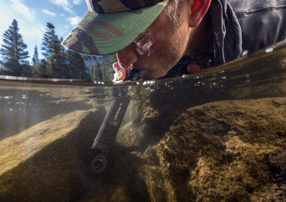 Mężczyzna używa filtra LifeStraw Peak Personal Dark Grey pijąc wodę bezpośrednio z&nbsp;rzeki